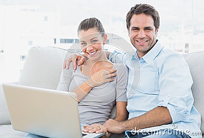 Happy couple sitting on the couch using laptop together
