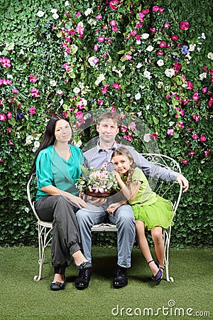 Happy family sit on bench with bunch of flowers