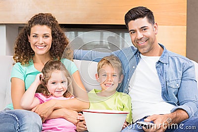 Happy family sitting on sofa watching tv with popcorn