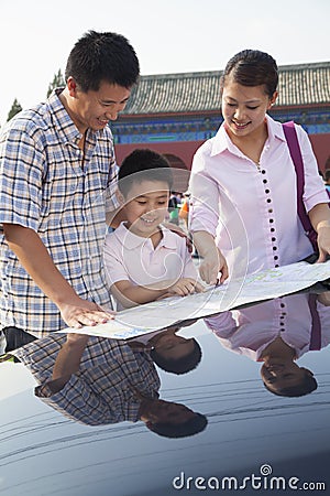 Happy family standing next to the car and looking down at the map