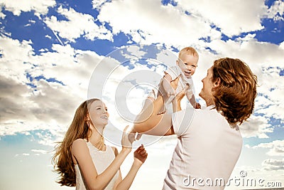 Happy family throws up baby boy against blue sky