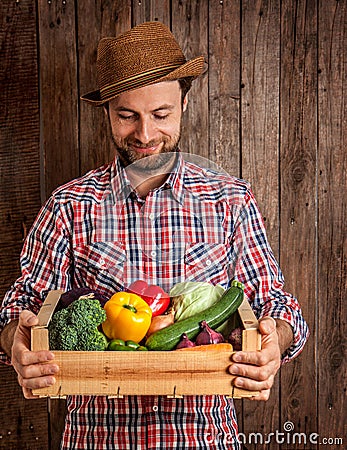 Happy farmer holding wooden box of vegetables