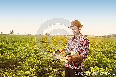 Happy farmer with vegetables in front of field landscape