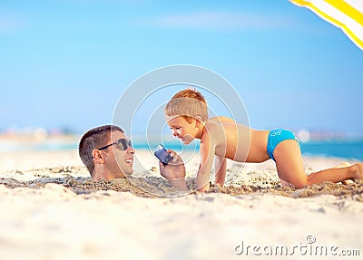 Happy father and son talking on smart phone together, on the beach
