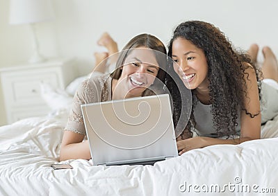 Happy Female Friends Using Laptop In Bed