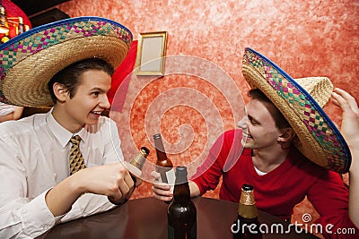 Happy friends wearing Mexican hats toasting at restaurant table
