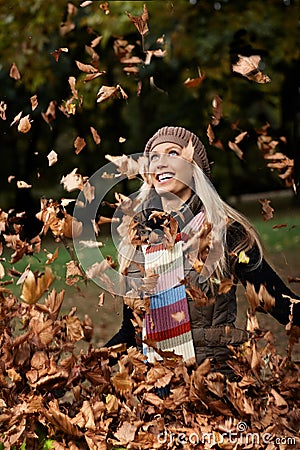 Happy girl among falling autumn leaves in park