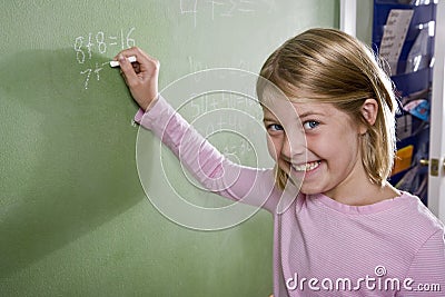 Happy girl writing math on blackboard in class