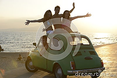 Happy group of friends with small car on beach