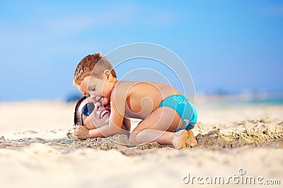 Happy kid hugging father s head in sand on the beach