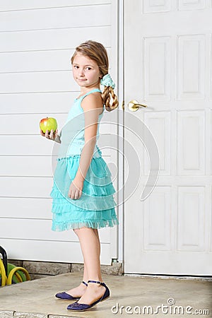 Happy little beautiful girl holds apple and stands white door