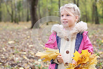 Happy little blonde girl holds yellow maple leafle