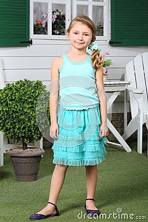 Happy little cute girl in skirt stands near cottage.