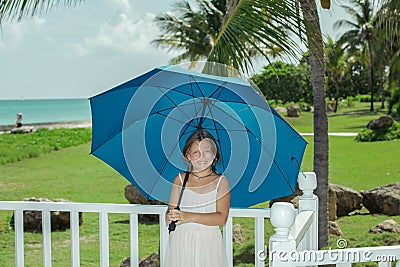 Happy little girl with blue umbrella enjoying her vacation time in cozy tropical garden