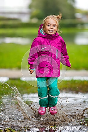 Happy little girl plays in a puddle