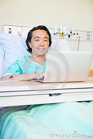 Happy Male Patient Using Laptop On Hospital Bed