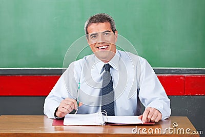 Happy Male Teacher With Pen And Binder Sitting At