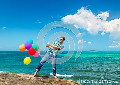 Happy man holding bunch of colorful air balloons at the beach