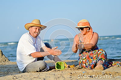 Happy mature couple having fun sitting at seashore on sandy beach