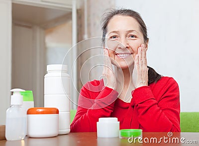 Happy mature woman puts cream on face