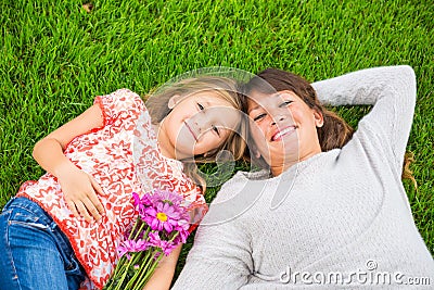 Happy mother and daughter relaxing outside on green grass. Spend