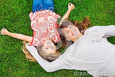 Happy mother and daughter relaxing outside on green grass. Spend