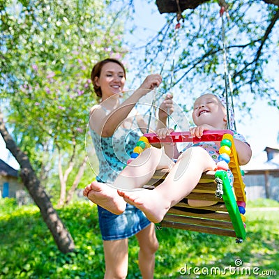 Happy mother rocking a laughing baby on a swing