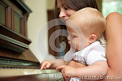 Happy mother teaching cute baby to play piano