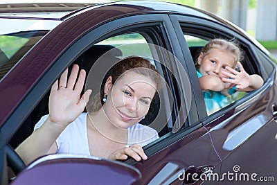 Happy mother and young daughter waving from car