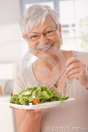 Happy old woman eating green salad