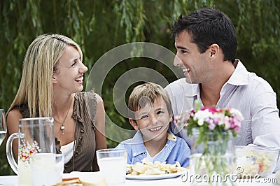 Happy Parents With Son Sitting At Dining Table In Garden