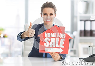 Happy realtor woman showing home for sale sign