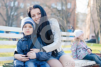 Happy smiling & looking at camera beautiful mother hugging or holding son young boy, sitting lonely one little girl