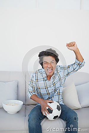 Happy soccer fan cheering while watching tv