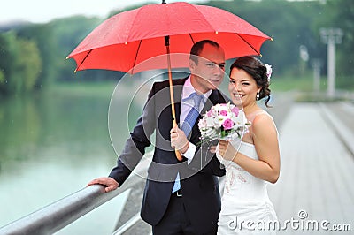 Happy wedding couple hiding from rain