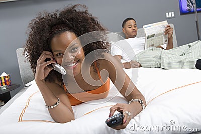 Happy Woman On Call While Watching TV In Bedroom