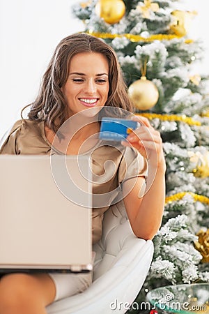 Happy woman with credit card using laptop near christmas tree