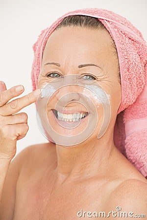Happy woman putting cream on face