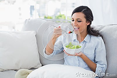 Happy woman relaxing on the sofa eating salad