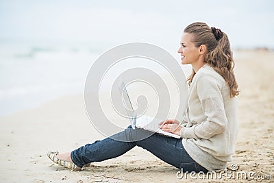 Happy woman sitting with laptop on cold beach