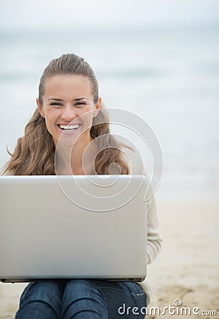 Happy woman sitting with laptop on cold beach