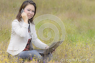 Happy woman talking on smartphone and working on laptop