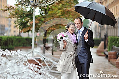 Happy young bride and groom on their wedding day by the rain