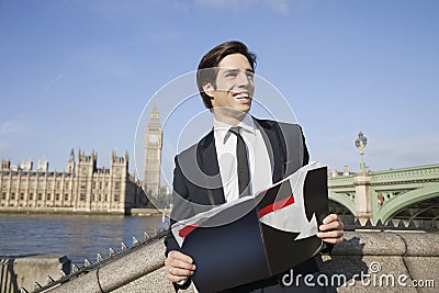 Happy young businessman with book standing against Big Ben clock tower, London, UK