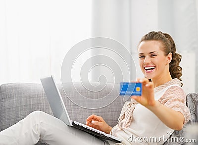 Happy young housewife with laptop showing credit card