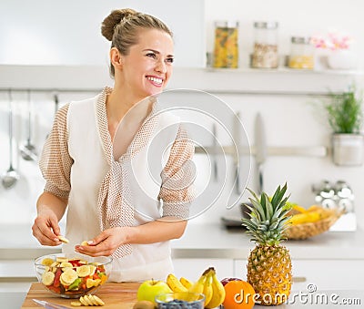 Happy young housewife making fruits salad