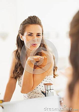 Happy young woman blowing air kiss in mirror in bathroom