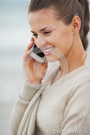 Happy young woman in sweater on beach talking cell phone