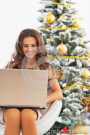Happy young woman using laptop near christmas tree