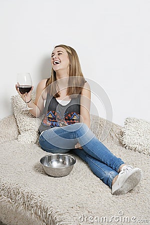 Happy young woman with wine glass sitting on sofa